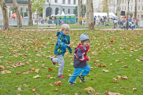 Otroka se igrata med jesenskim listjem v parku